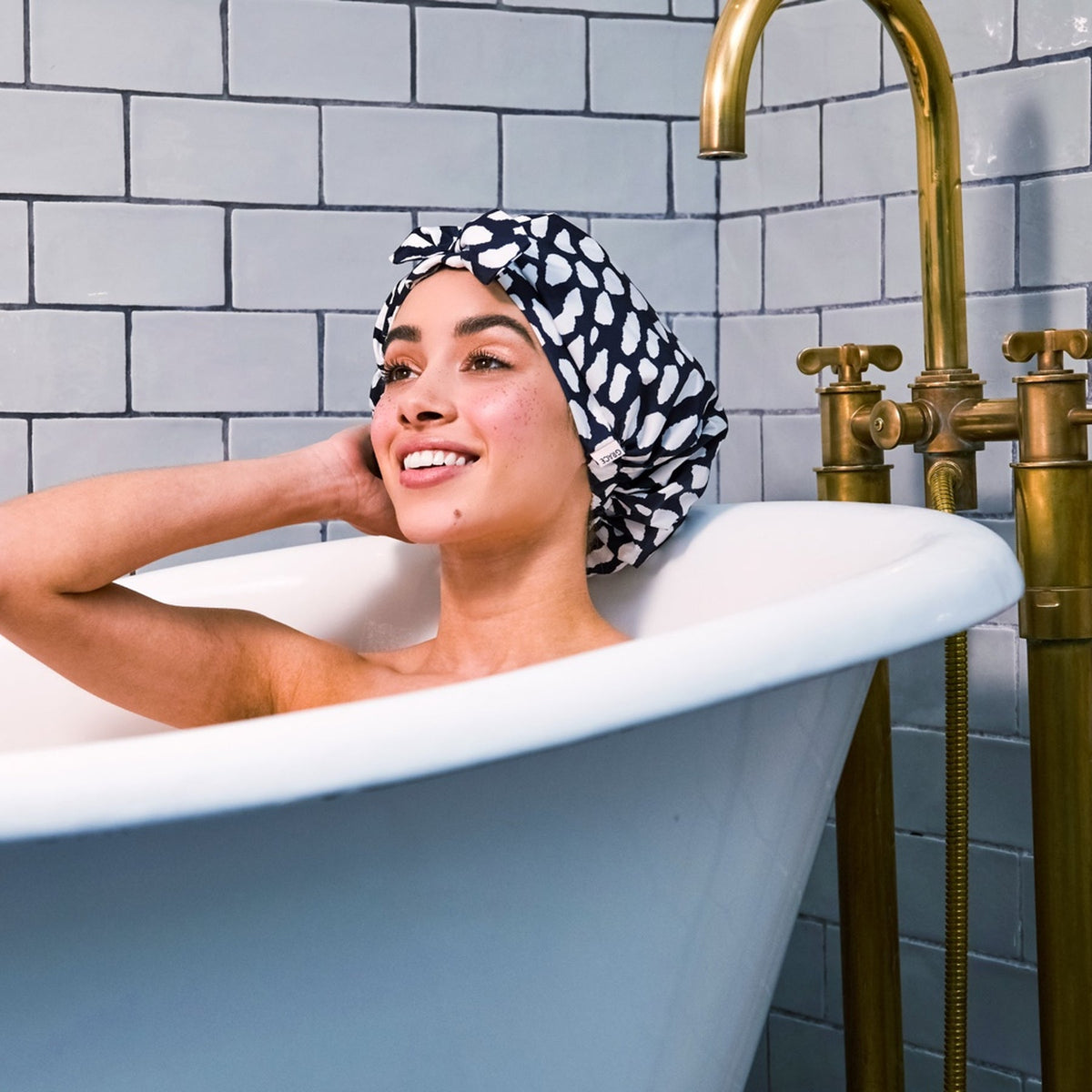 Model relaxing in bathtub wearing Grace & Company Casablanca shower cap, with shower cap visible